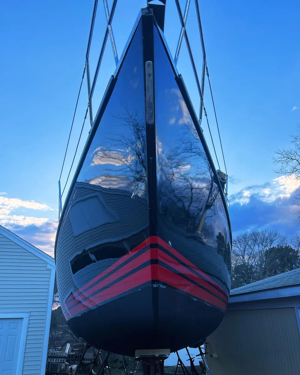 Freshly buffed black sailboat hull with red boot stripes, on stands in the yard