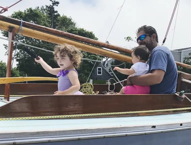 Renan Pinto sailing a wooden boat with his two young daughters